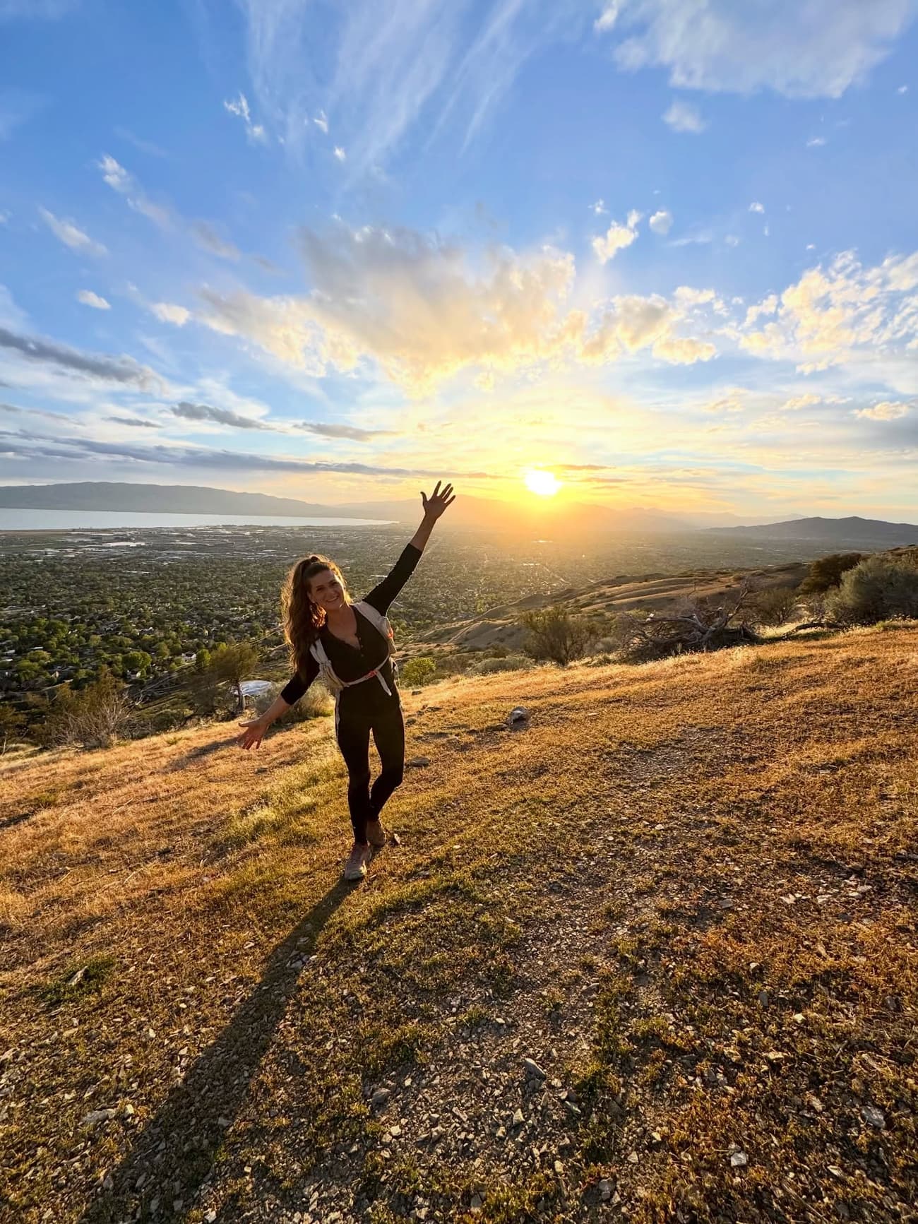 Sarah Heiner on a golden foothill trail at sunset, arms raised